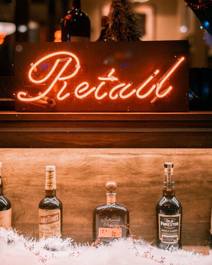 Illuminated bar scene with neon retro sign and alcohol bottles lined up on a shelf.